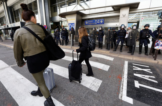 Hành khách kéo hành lý đi bộ qua nhà ga số 1 tại sân bay Nice, Pháp trong bối cảnh cảnh sát chống bạo động đứng xung quanh ngày 23/3. Ảnh: Reuters