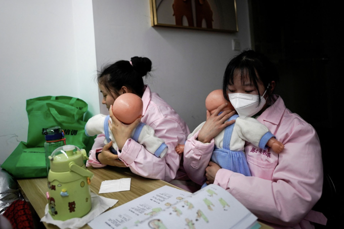 Hai phụ nữ trẻ thực hành cách bế mô hình trẻ sơ sinh theo hướng dẫn trong giáo trình, tháng 3/2023. Ảnh: REUTERS/Aly Song